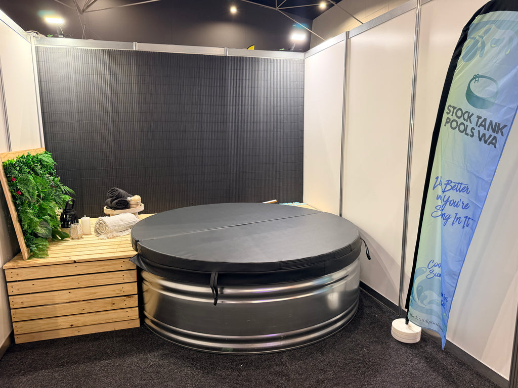 A circular metal stock tank with a dark gray fitted cover, displayed inside a booth at the home expo perth with vertical banner reading Stock Tank Pools Wa.